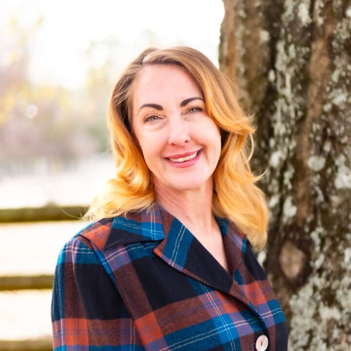 A woman in plaid shirt standing next to tree.
