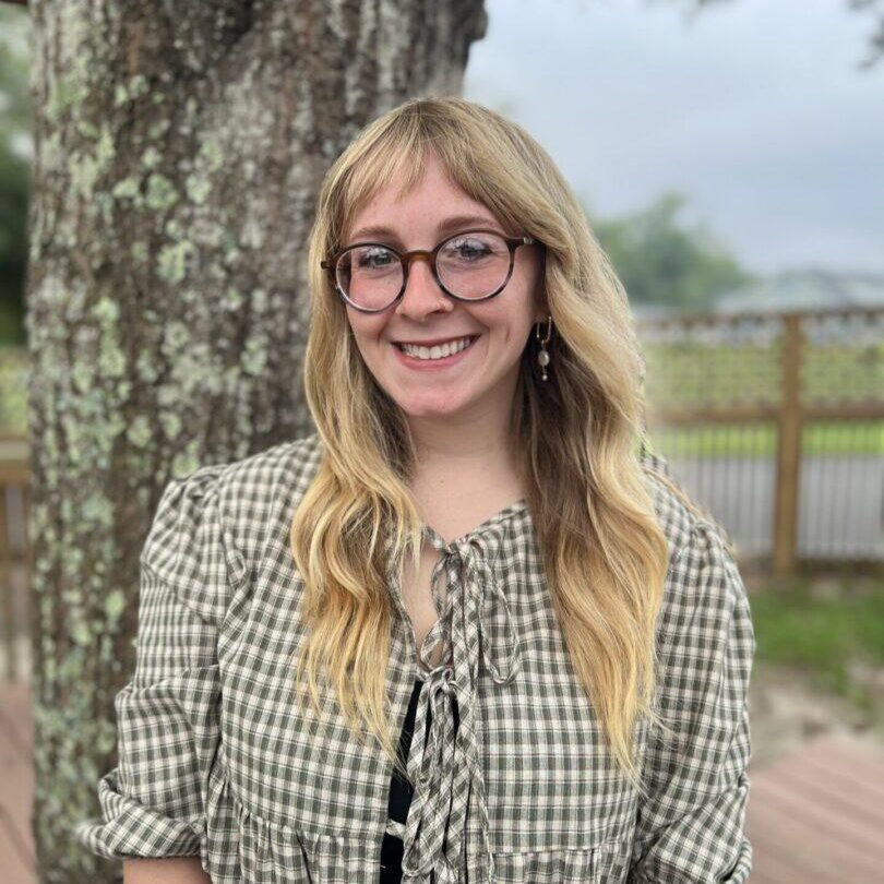 Smiling woman with glasses by a tree.